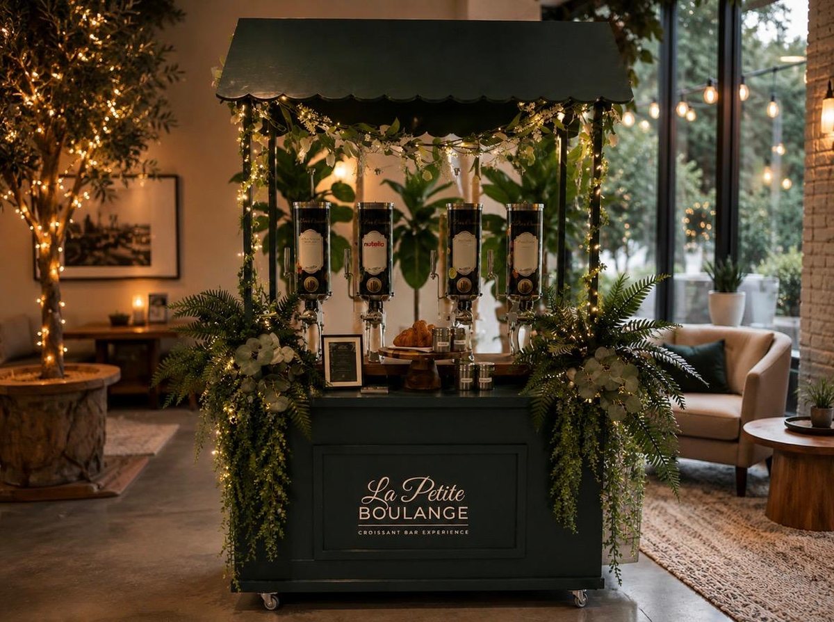 The La Petite Boulange croissant cart styled with greenery and string lights at an evening wedding
